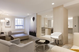 Un salon moderne avec un canapé, des fauteuils, une table basse et une vue sur le paysage urbain, visible à travers une grande fenêtre.