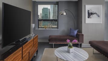 A modern living room with a large flat-screen TV, a sofa, a coffee table with flowers, and a city view through a window.