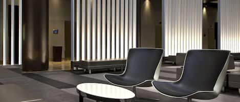 A modern lobby with two black chairs, a small round table, and vertical light panels.