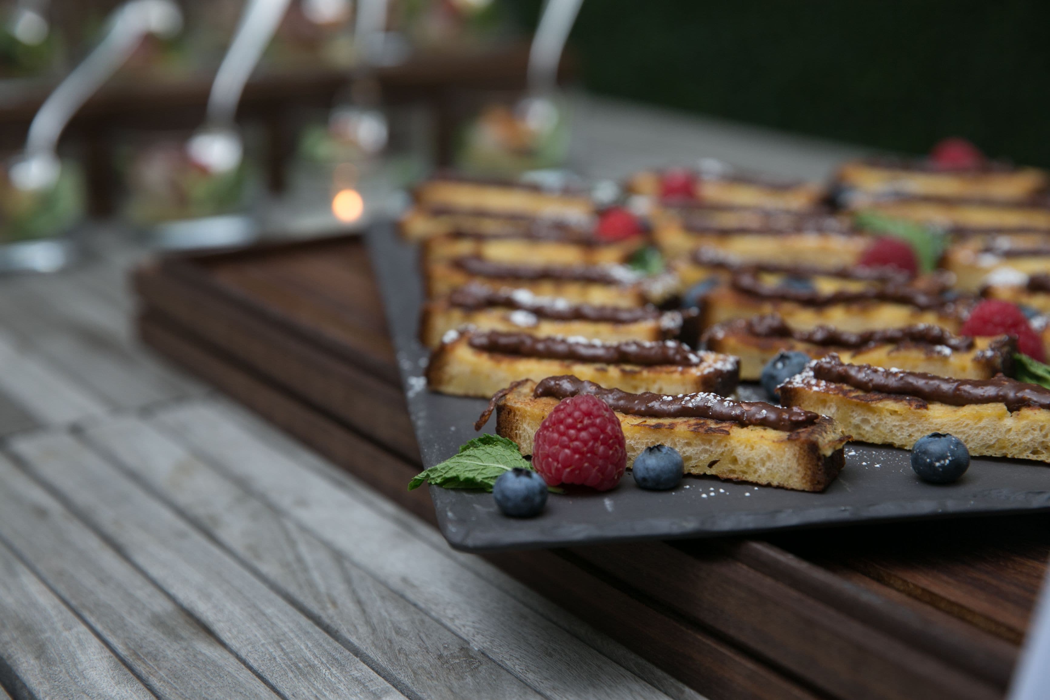A dessert tray with chocolate-topped pastries, berries, and mint leaves on a slate board.