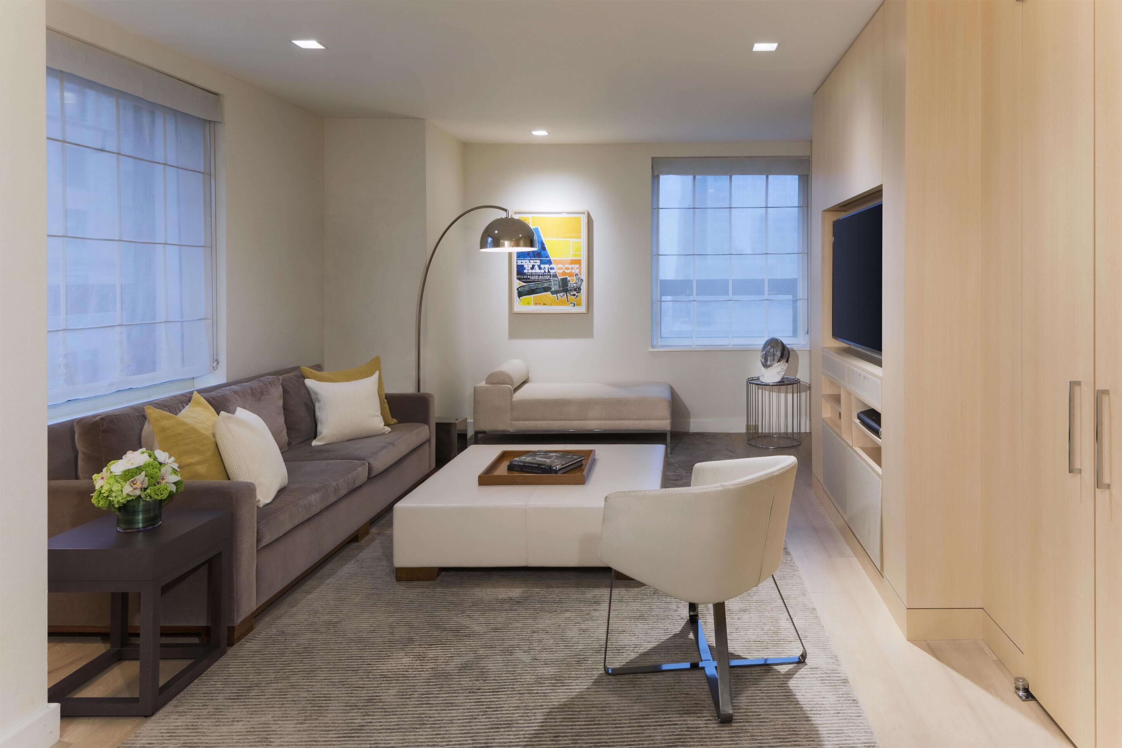 Una sala de estar moderna con sofá, mesa de centro y sillón, televisión y una obra de arte en la pared.