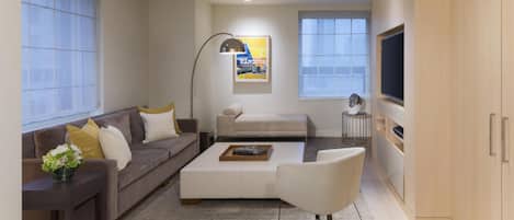 Una sala de estar moderna con sofá, mesa de centro y sillón, televisión y una obra de arte en la pared.