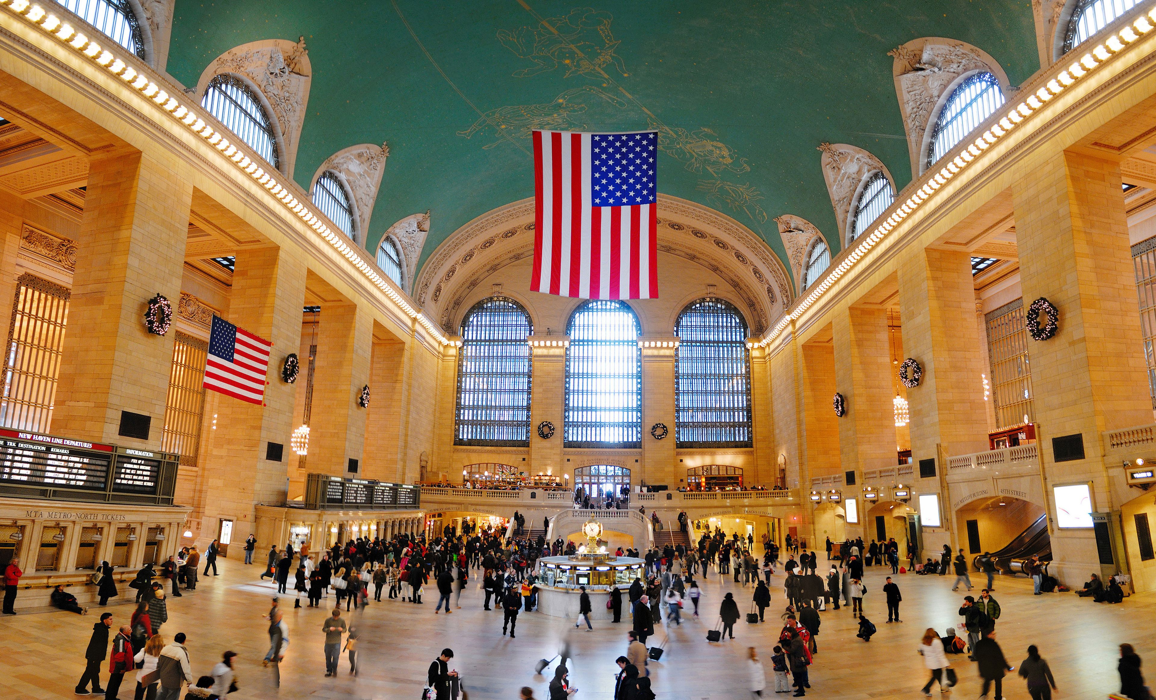 A spacious train station with high ceilings, large windows, and an American flag.