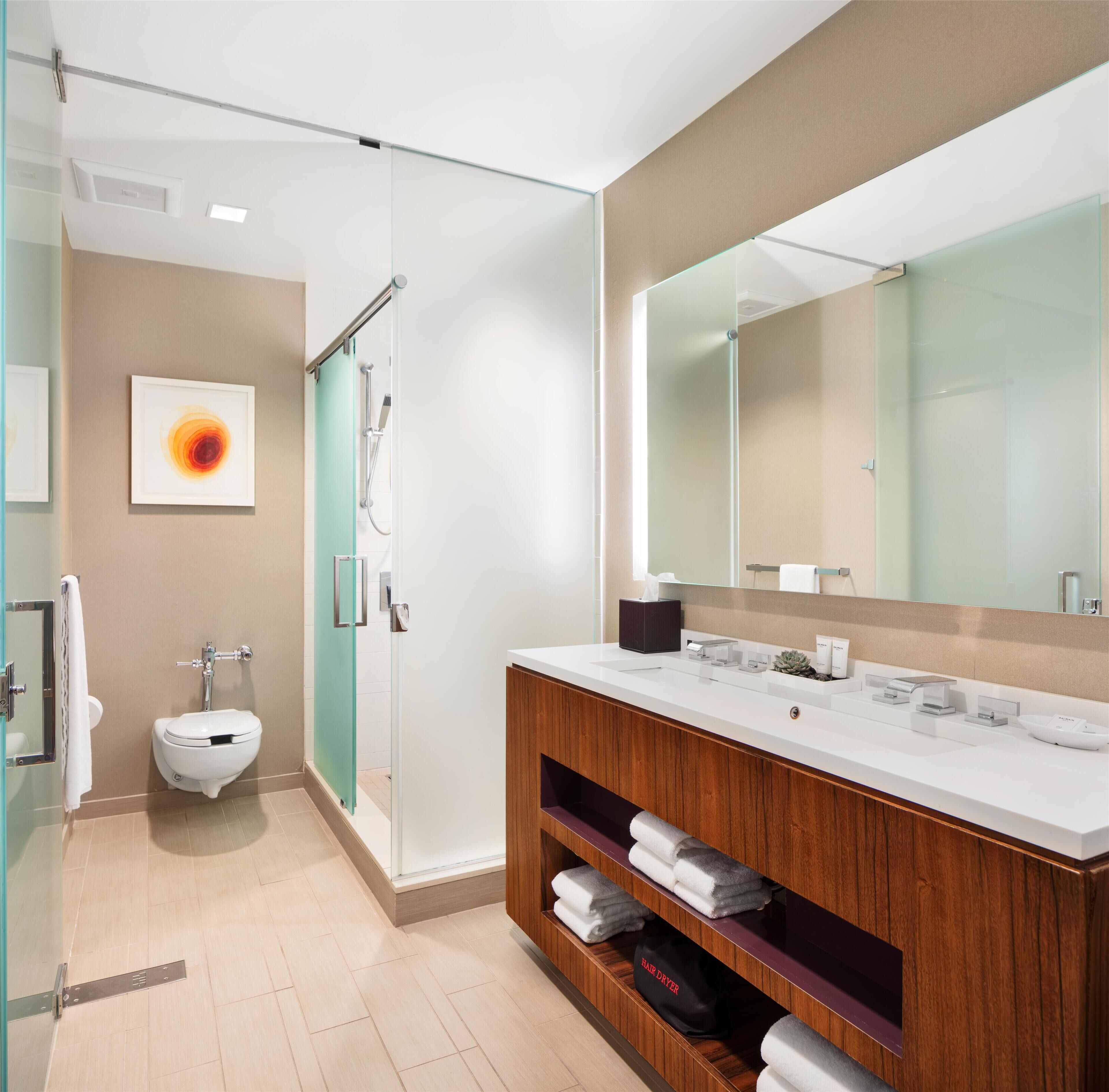 Un baño moderno con cabina de ducha de vidrio, inodoro blanco, tocador con espejo y toallero.
