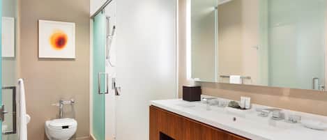 Un baño moderno con cabina de ducha de vidrio, inodoro blanco, tocador con espejo y toallero.