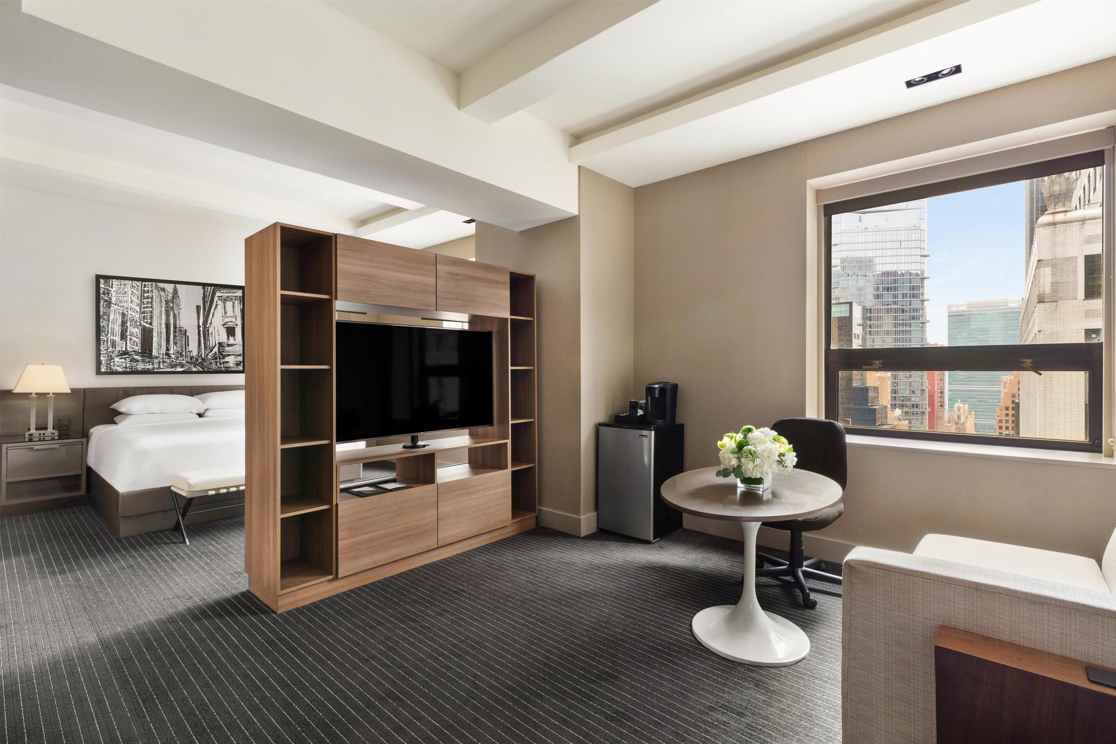 Habitación de hotel con cama, televisión, escritorio y silla, y ventana con vista a la ciudad.