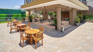 Un patio al aire libre con mesas y sillas de madera, un espacio de estar cubierto y plantas en macetas.
