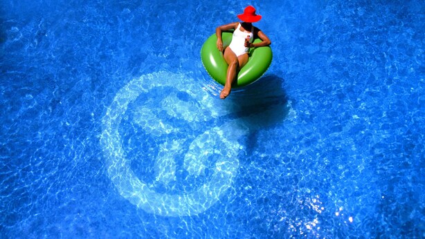 Una persona con traje de baño y sombrero rojo sentada sobre un flotador verde en una piscina.