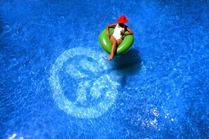 Una persona con traje de baño y sombrero rojo sentada sobre un flotador verde en una piscina.