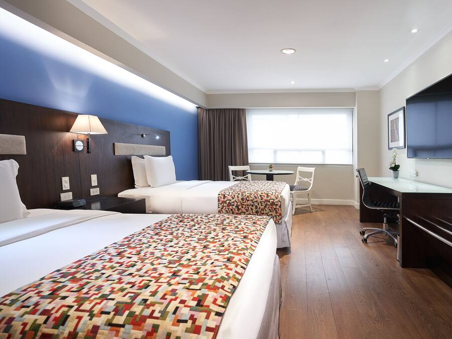 Habitación de hotel con dos camas, un escritorio, una silla, un televisor y una ventana con cortinas.