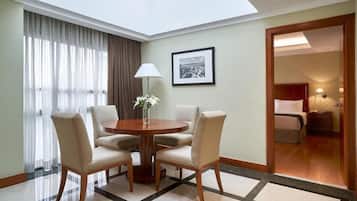 A hotel room with a round dining table, four chairs, a lamp, a framed picture on the wall, and a bed with a nightstand.