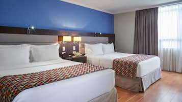 A hotel room with two beds, a nightstand with a phone, and a window with curtains.