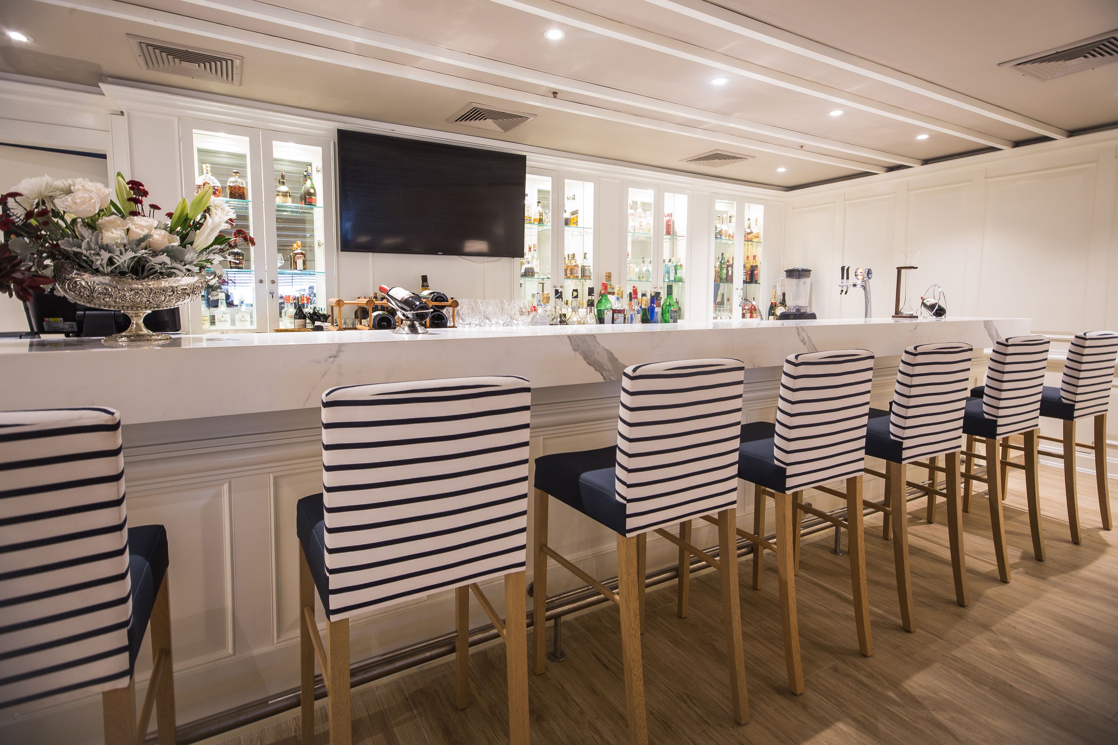A bar area with striped chairs, a flat-screen TV, and a variety of bottles.