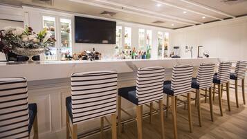 A bar area with striped chairs, a flat-screen TV, and a variety of bottles.