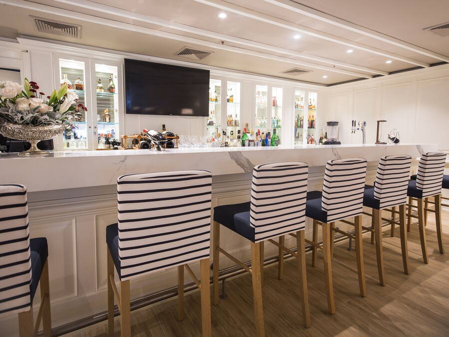 A bar area with striped chairs, a flat-screen TV, and a variety of bottles.