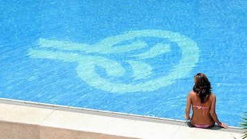 A woman in a bikini sitting by a pool with a large blue logo on the water.