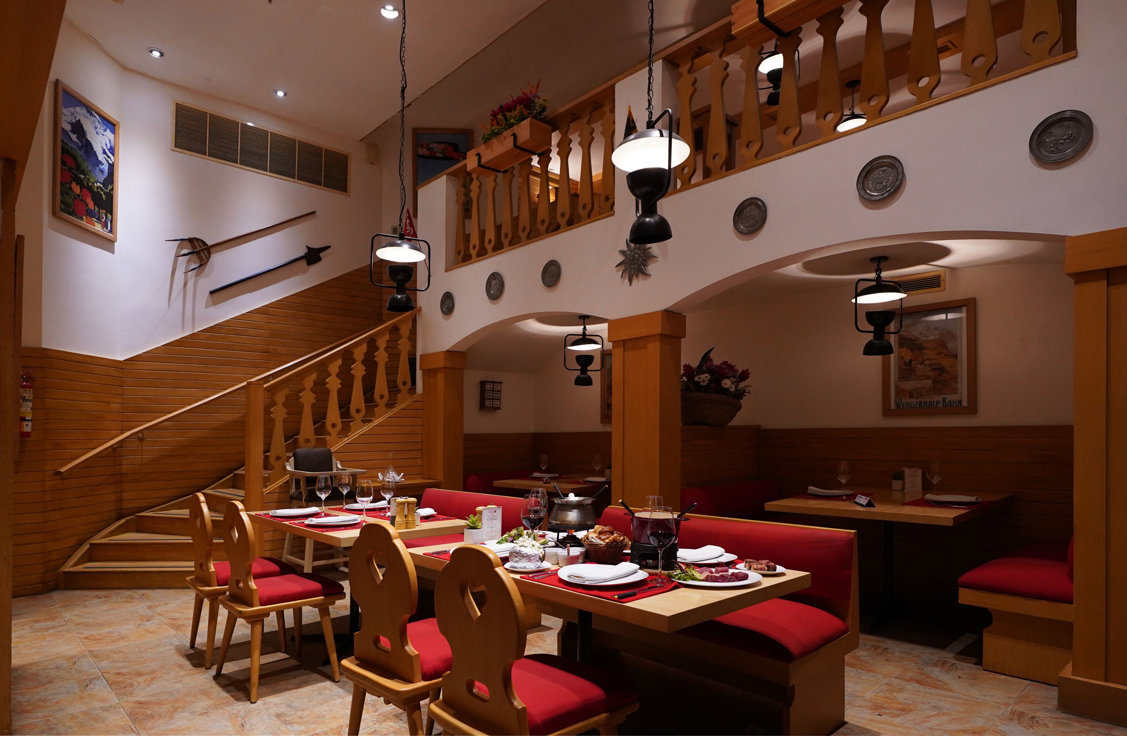 A restaurant with wooden furniture, red cushions, and a staircase.
