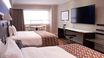 A hotel room with two beds, a desk, a chair, a TV, and a window with curtains.