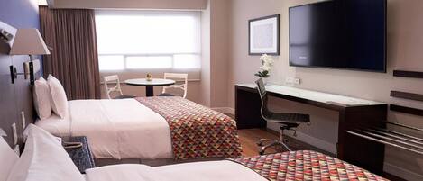 A hotel room with two beds, a desk, a chair, a TV, and a window with curtains.