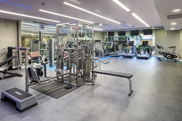 Un gimnasio moderno con diversos equipos de ejercicio, incluyendo cintas de correr, máquinas de pesas y una plataforma elevada.