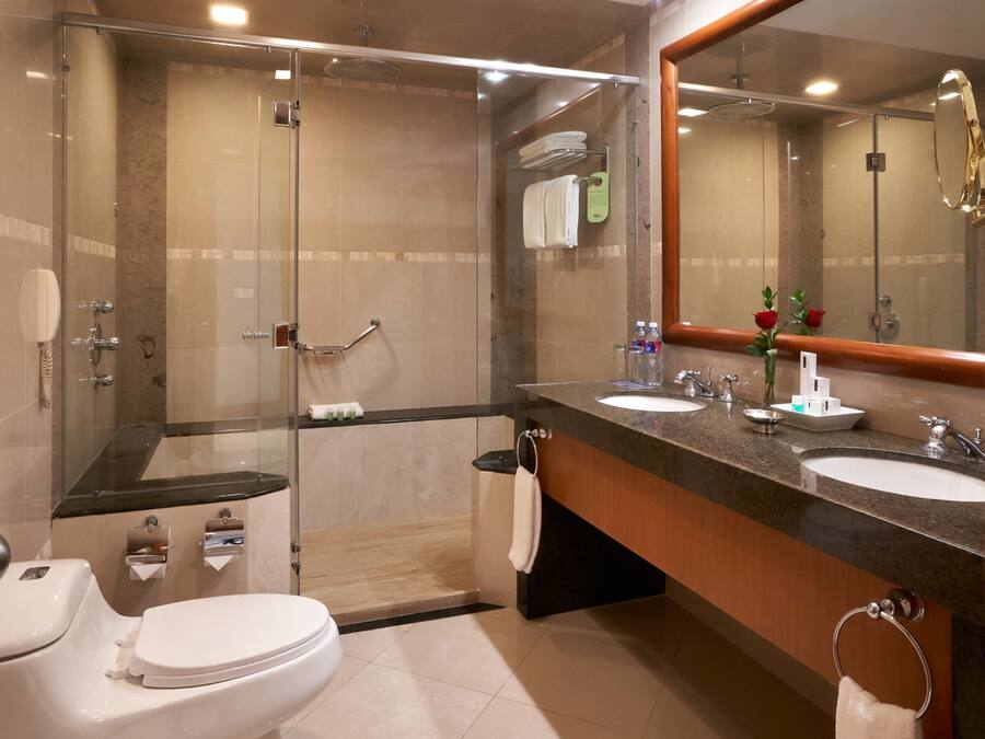 Un baño moderno con ducha de vidrio, dos lavamanos y un espejo grande.