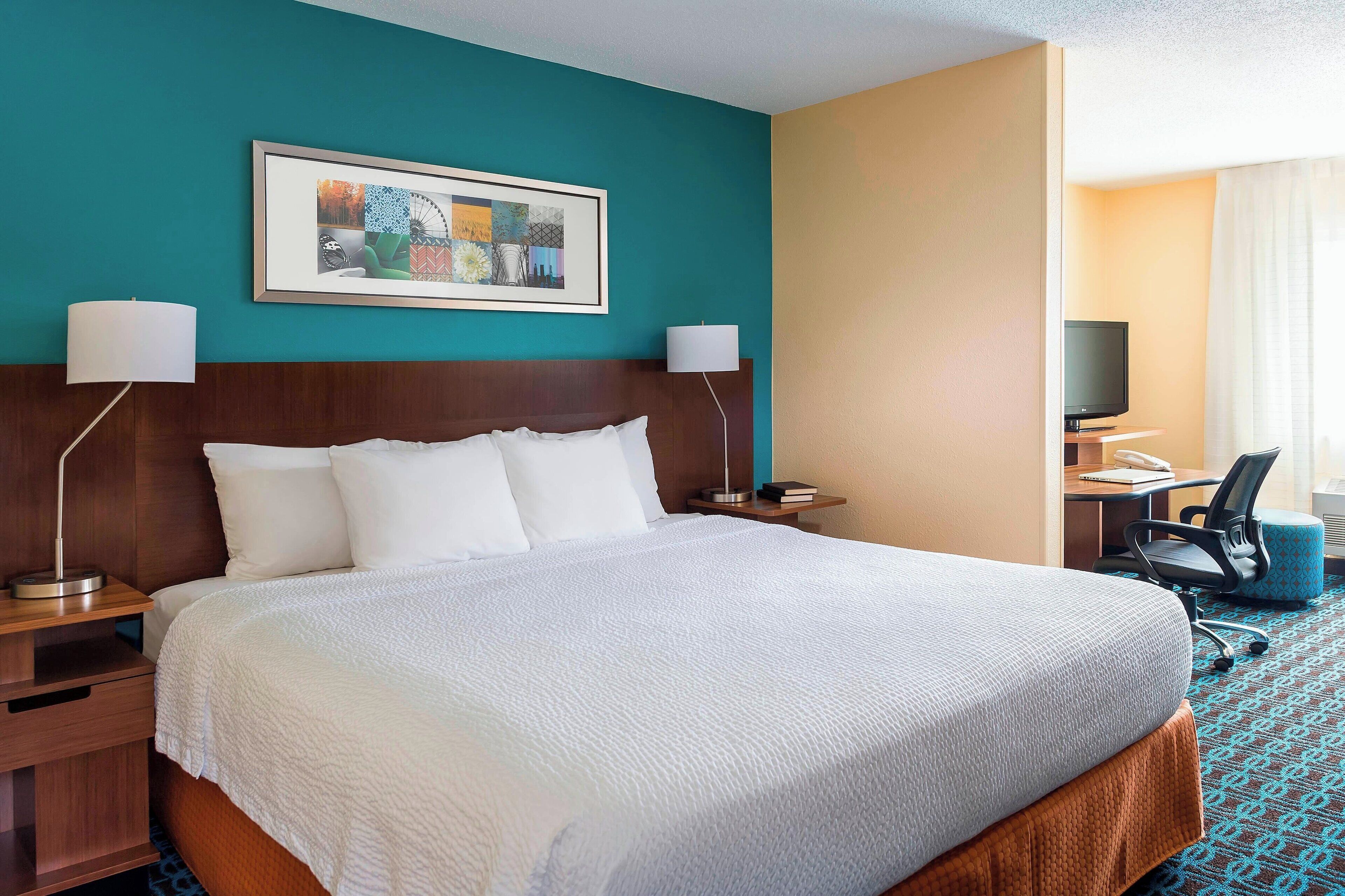 A hotel room with a large bed, two bedside tables, a desk with a chair, a television, and a framed artwork on the wall.