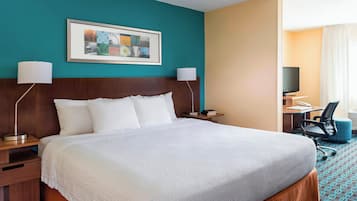 A hotel room with a large bed, two bedside tables, a desk with a chair, a television, and a framed artwork on the wall.