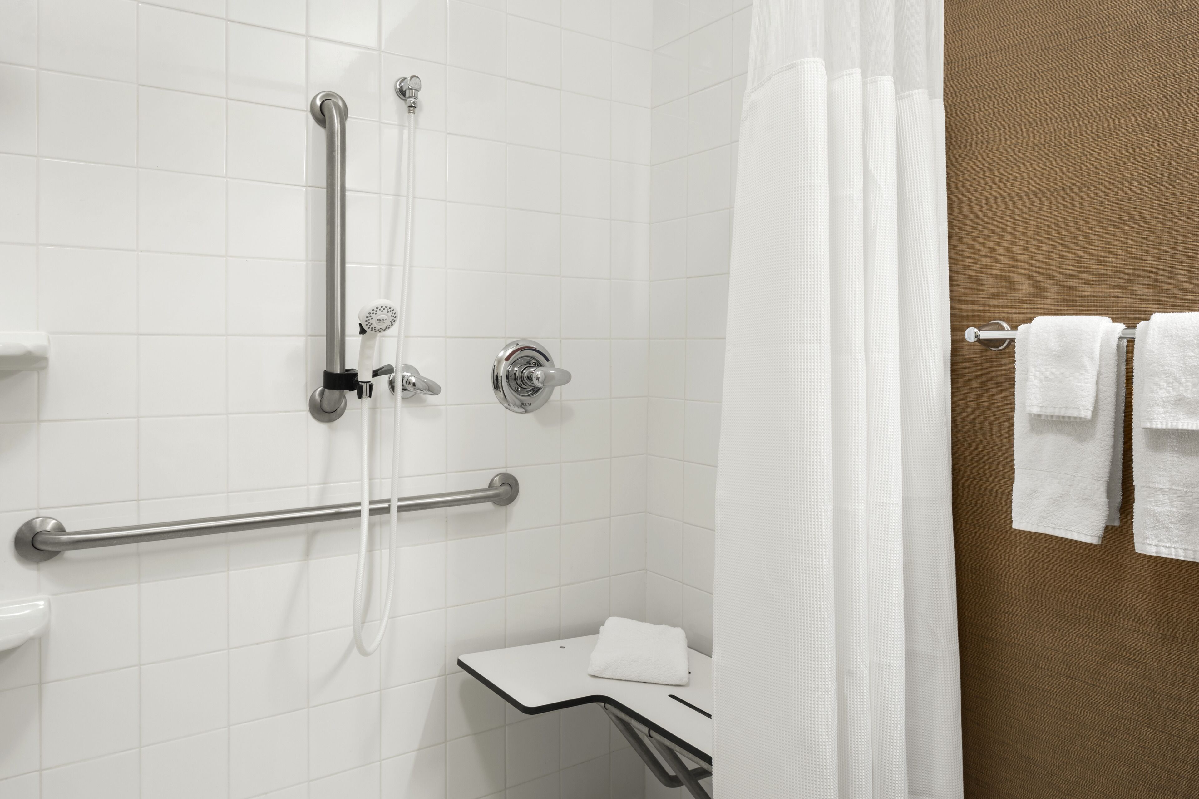 A shower area with a grab bar, a towel rack, and a white curtain.