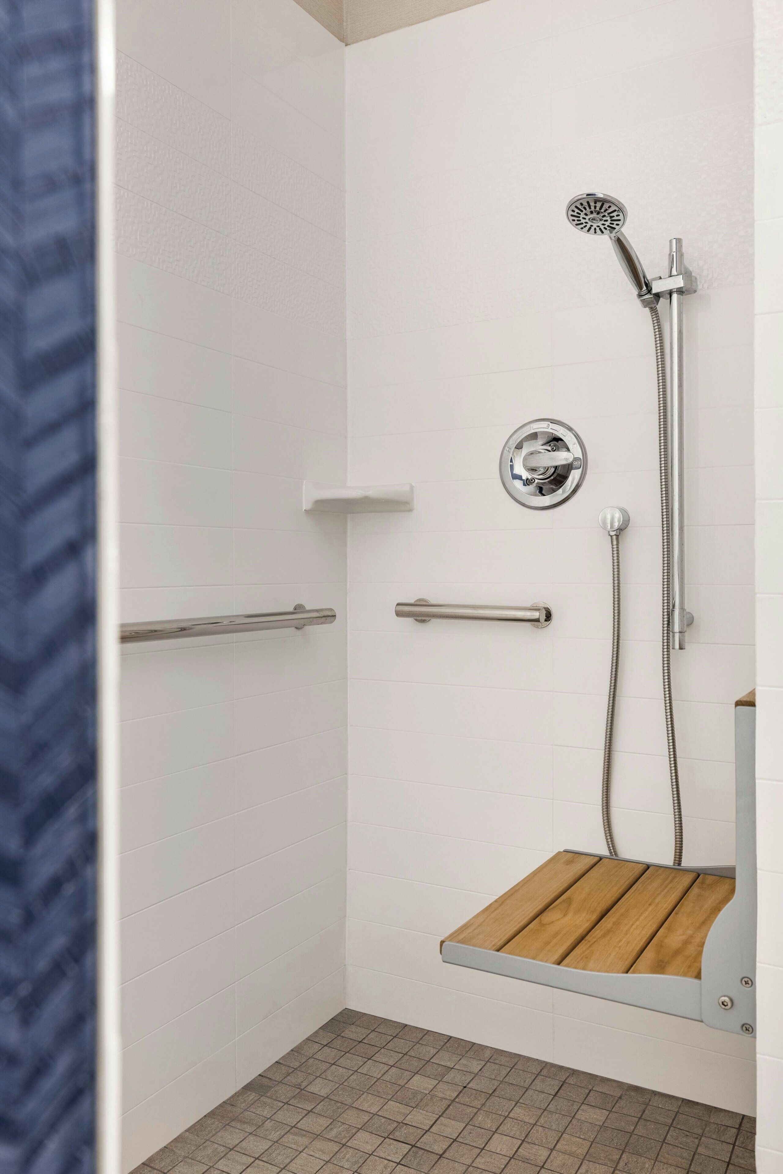 A shower area with a wooden step, a handheld showerhead, and a wall-mounted control panel.