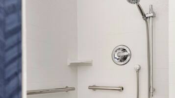 A shower area with a wooden step, a handheld showerhead, and a wall-mounted control panel.