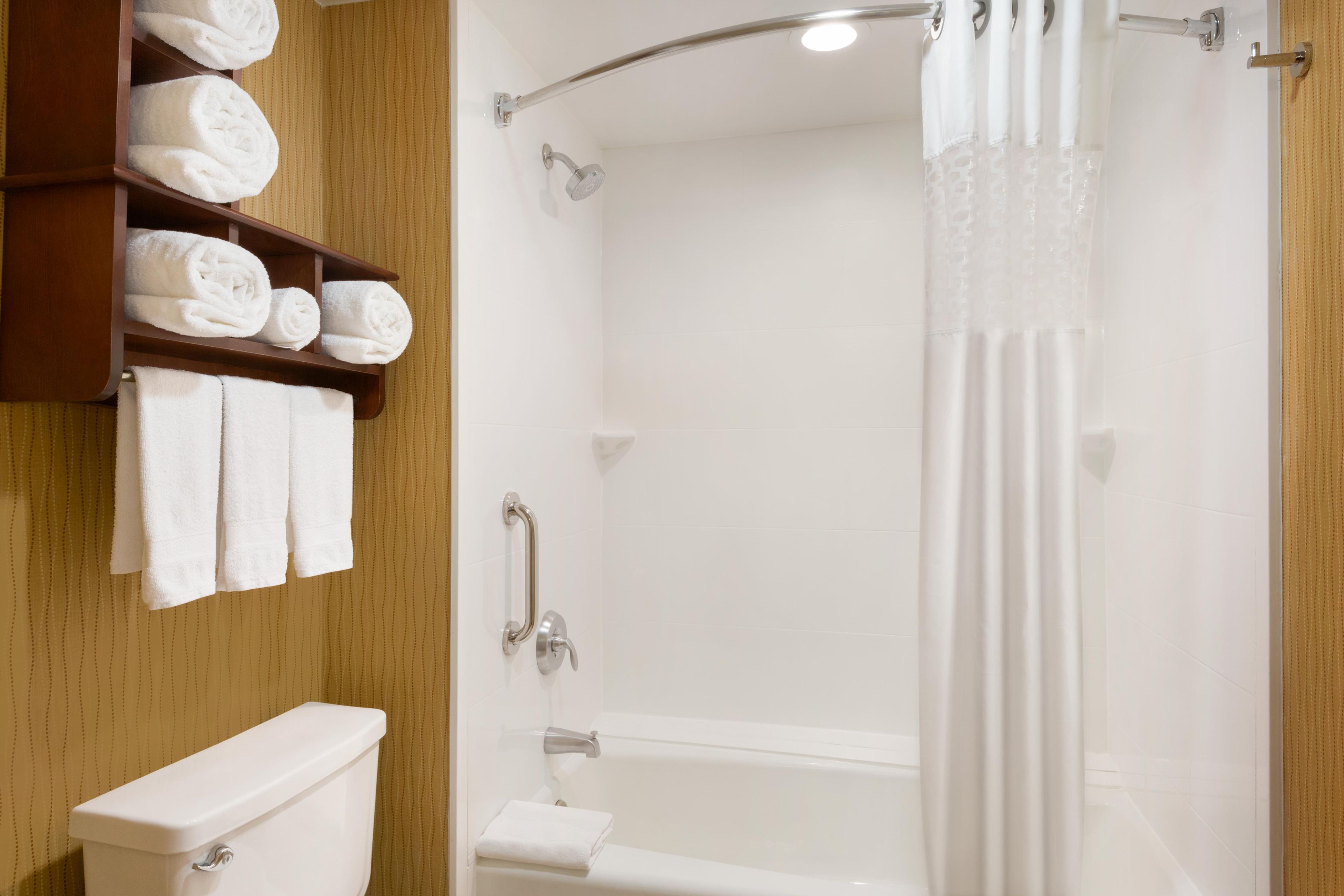 Un baño con inodoro, ducha con puerta de vidrio y un perchero con toallas dobladas.