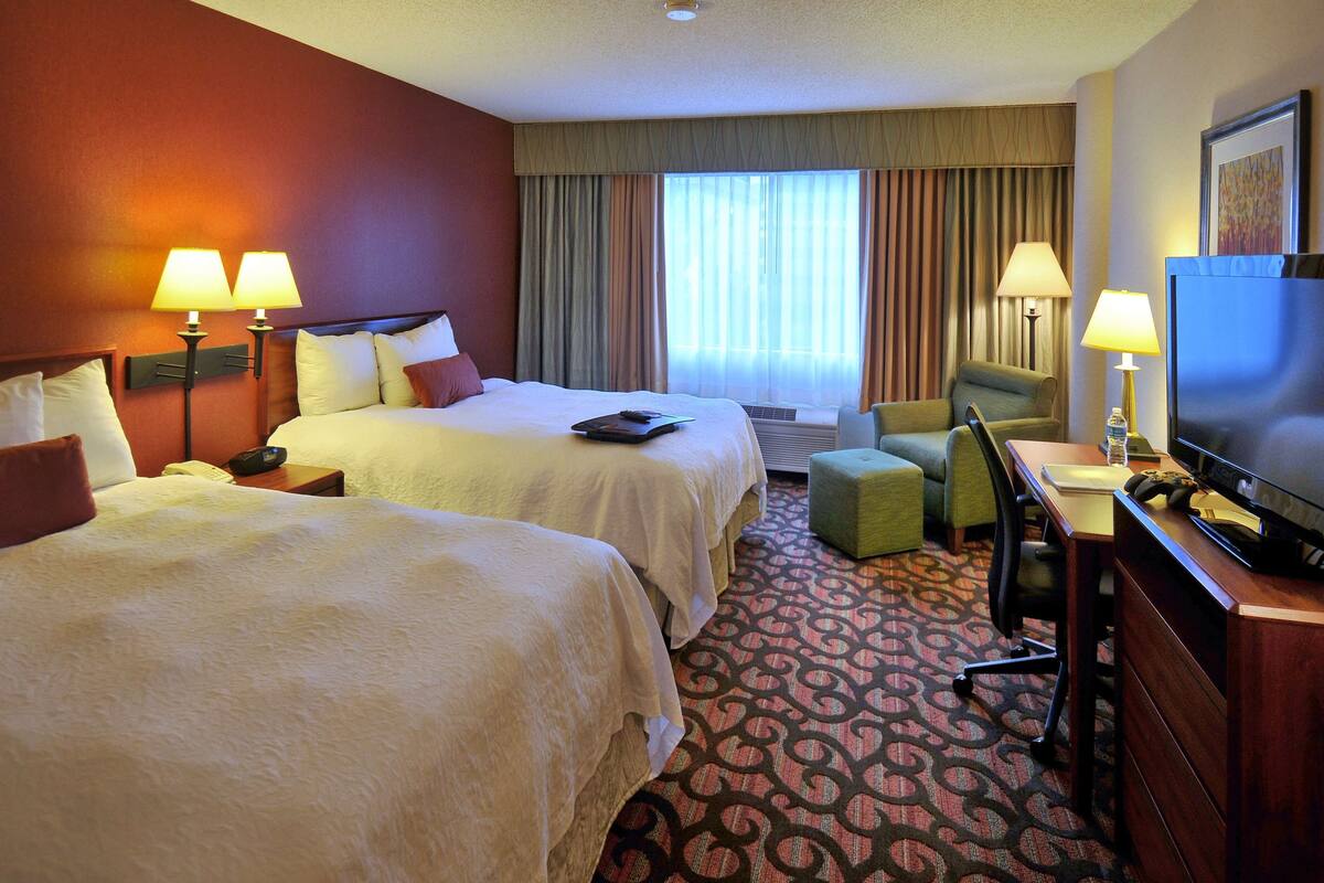 A hotel room with two beds, a desk with a television, a chair, and a desk lamp.