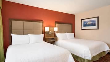 Quarto de hotel com duas camas, uma mesa de cabeceira com abajur, um quadro na parede e um tapete vermelho.