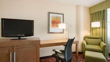 Habitación de hotel con escritorio, televisión, silla e imagen enmarcada en la pared.