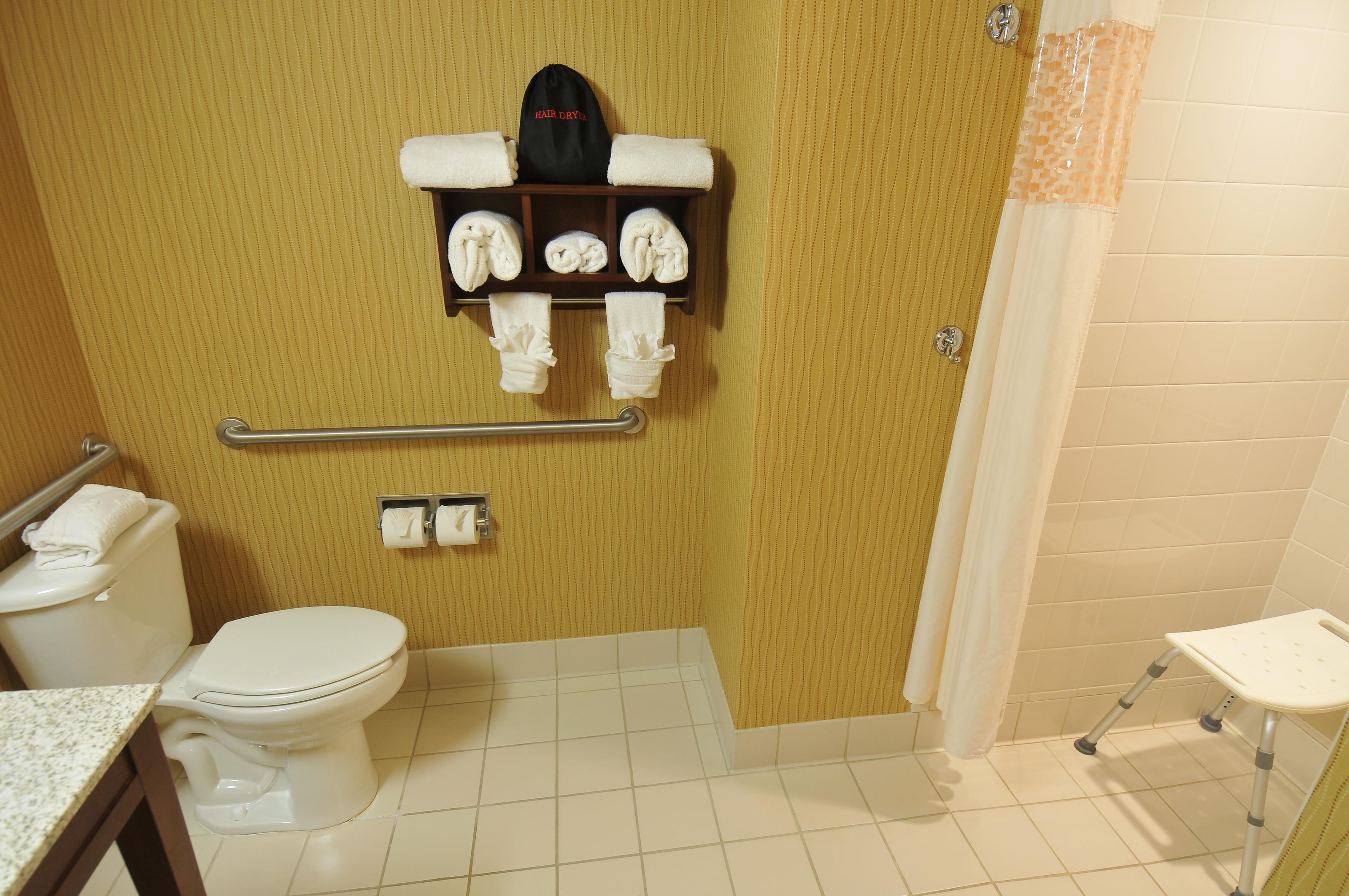 A bathroom with a toilet, a towel rack with towels, a hair dryer, and a shower area.