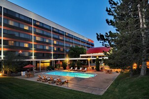 Un hotel con piscina, asientos al aire libre y un edificio de techo rojo.