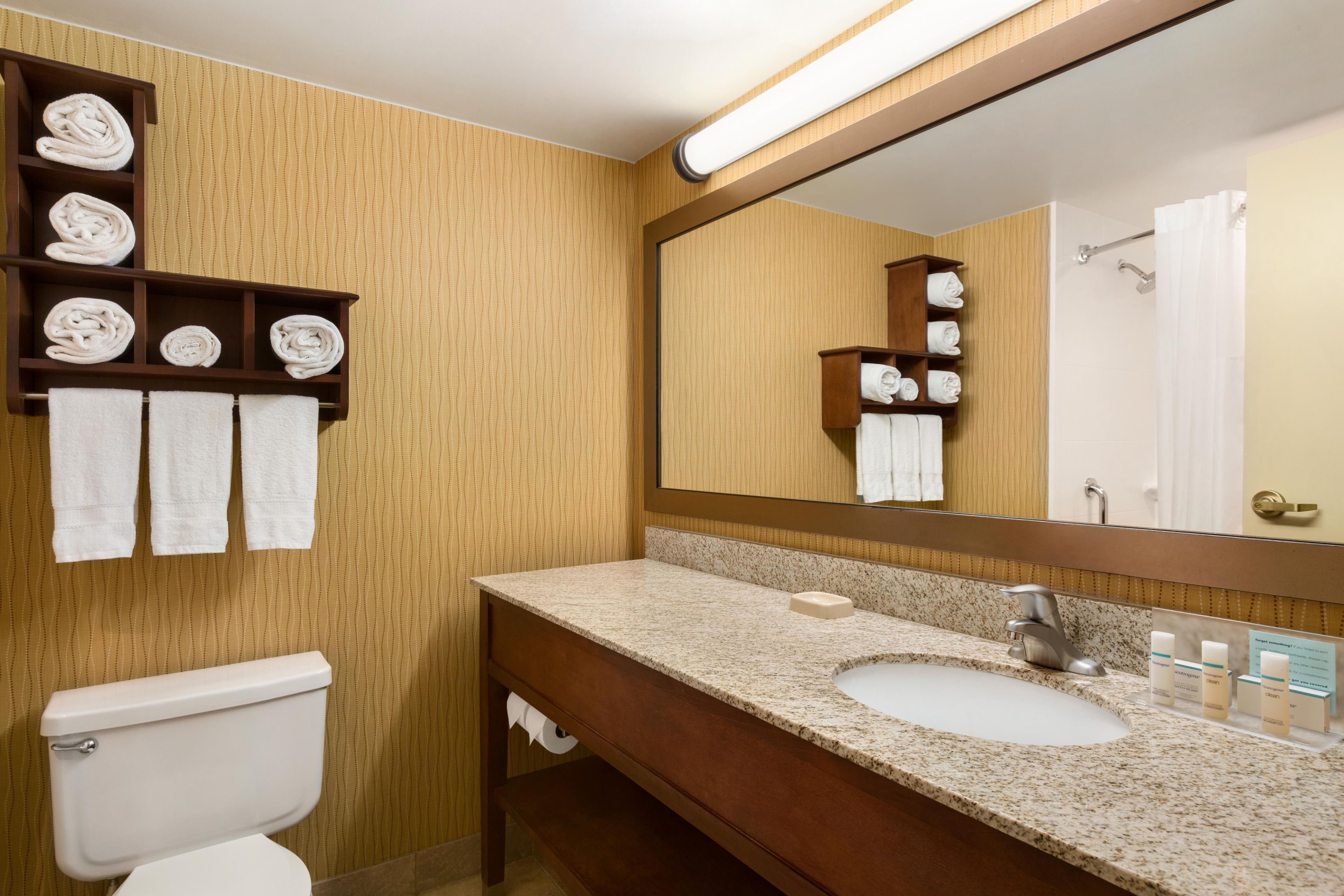 A bathroom with a toilet, a sink, and a mirror. There are shelves with towels and a shower curtain.