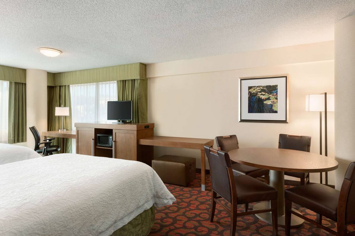 A hotel room with a bed, a desk with a television, a dining table with chairs, a small sofa, and a framed picture on the wall.