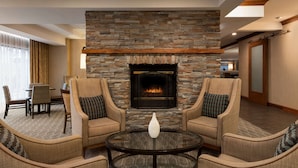 A lobby with a stone fireplace, two armchairs, a round table, and a dining area. - Hampton Inn Denver West Federal Center (Lakewood)