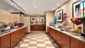 A hotel kitchen with checkered flooring, wooden cabinets, and various breakfast items on the counter. - Hampton Inn Denver West Federal Center (Lakewood)