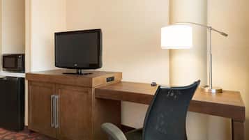 A hotel room with a wooden desk, a television, a lamp, a microwave, and a chair.