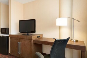A hotel room with a wooden desk, a television, a lamp, a microwave, and a chair.