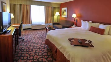 Una habitación de hotel con una cama, un escritorio con televisor, una silla y una lámpara de escritorio.