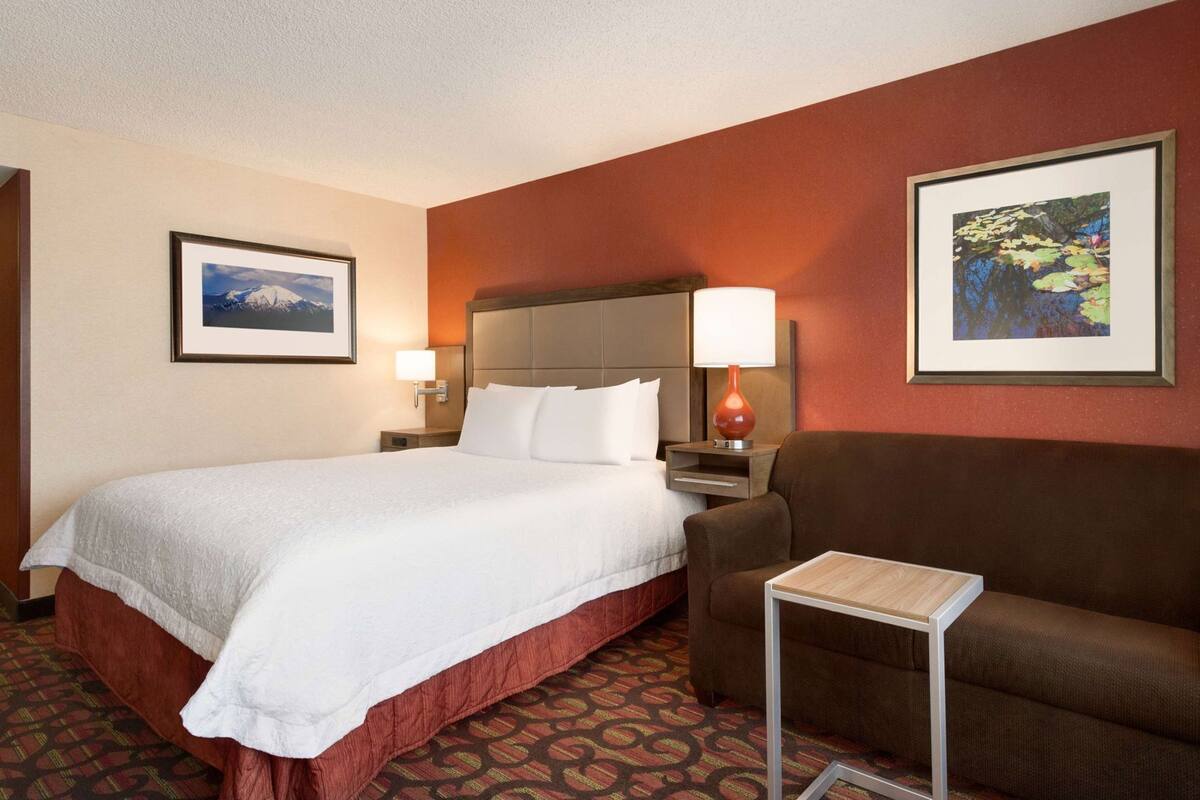 A hotel room with a bed, a brown sofa, a small table, and two wall-mounted lamps.