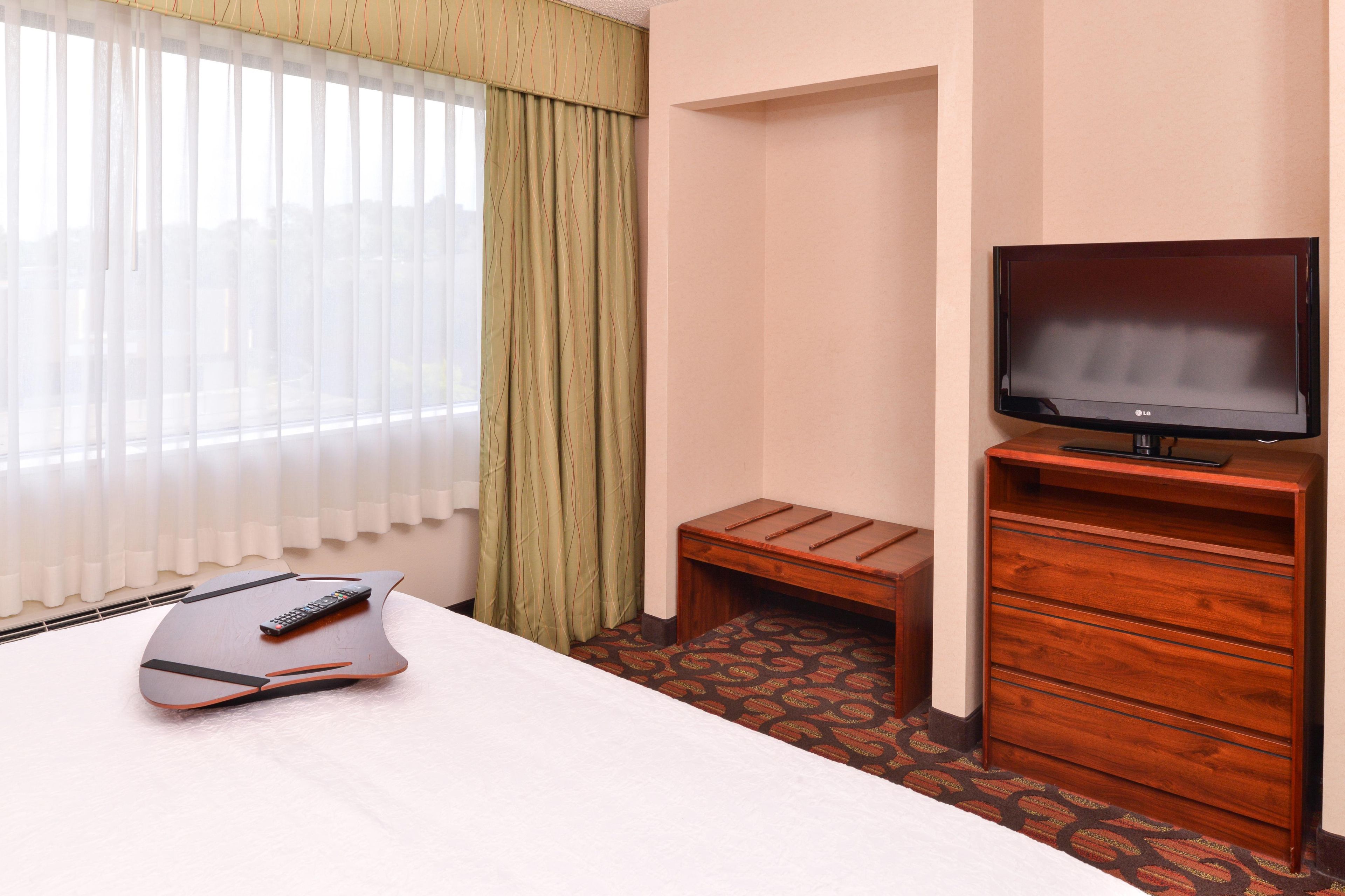Ein Hotelzimmer mit einem Bett, einem Fernseher auf einem Holzboden, einem kleinen Hocker und einer Fernbedienung auf dem Bett.