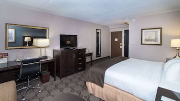 A hotel room with a bed, desk, chair, television, and a mirror.