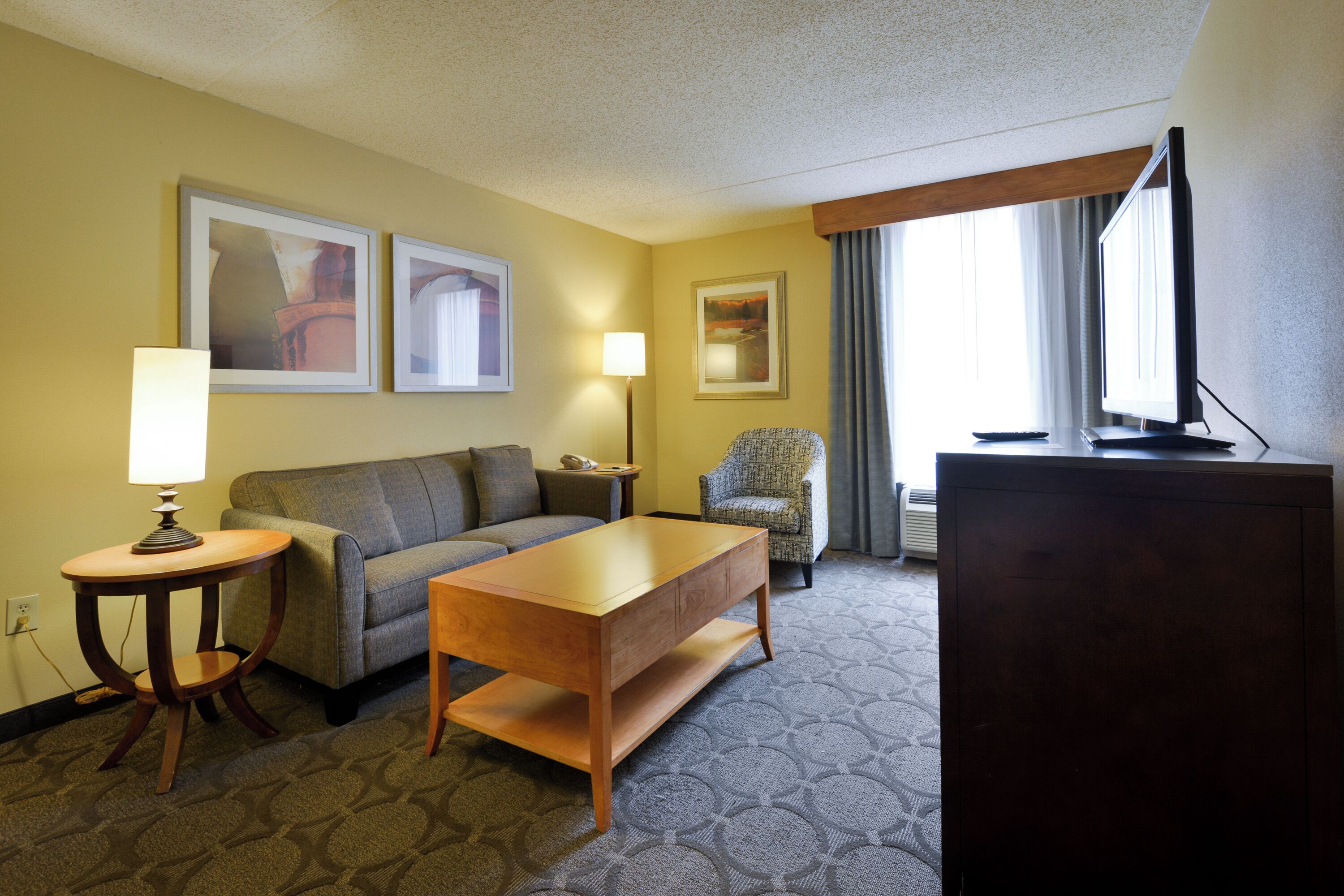 A hotel room with a sofa, a wooden coffee table, a television, and two lamps.