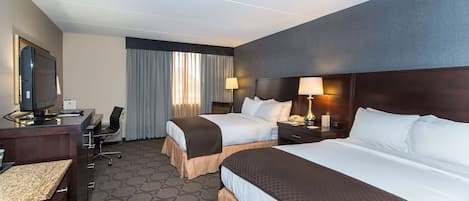 A hotel room with two beds, a desk, a chair, a TV, and a window with curtains.