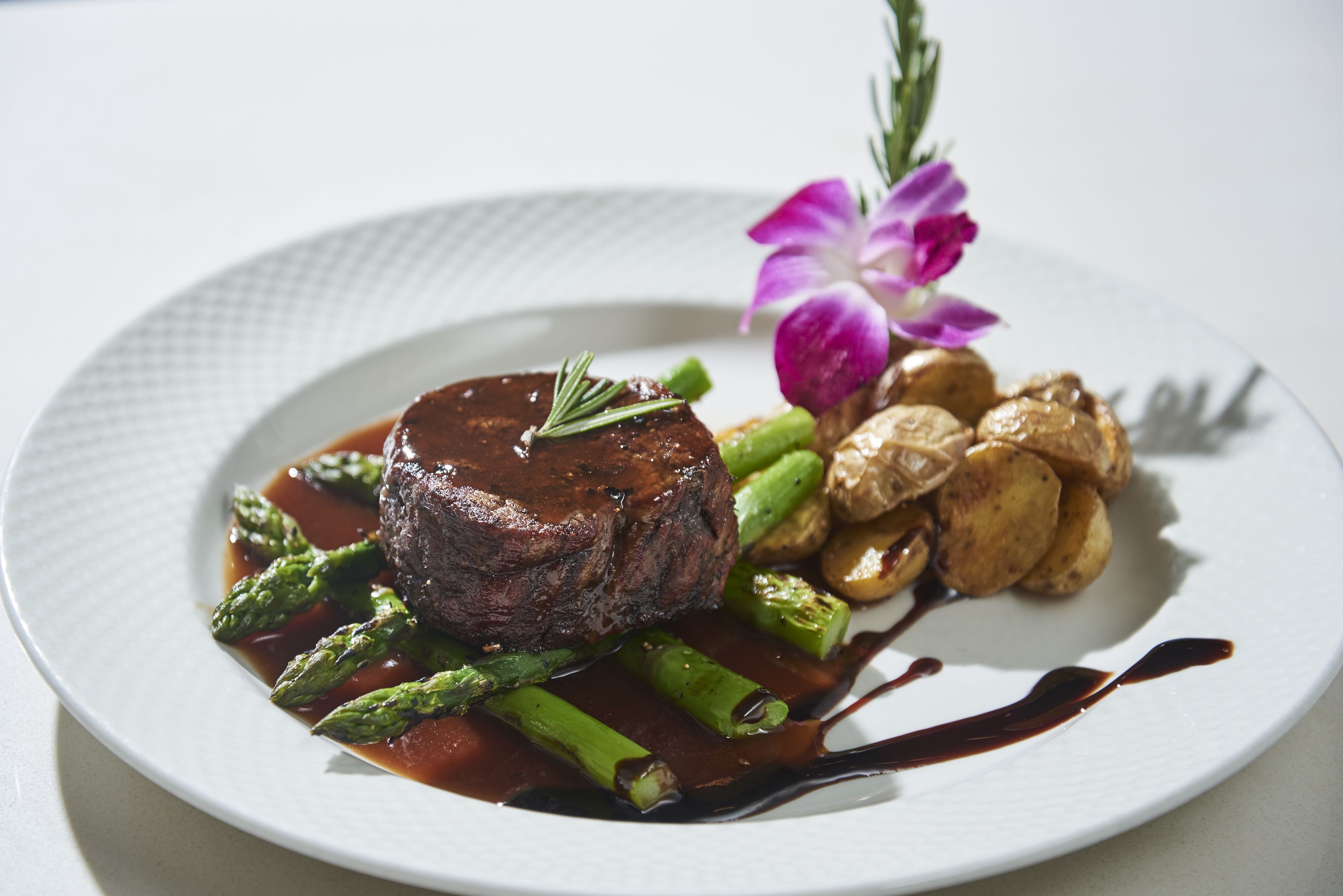 A plate of food with a steak, asparagus, and potatoes, garnished with a flower.