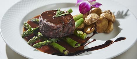 Prato de comida com bife, aspargos e batatas, decorado com uma flor.